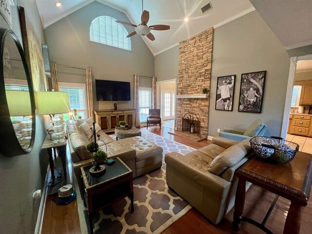 living room with ceiling fan, a fireplace, hardwood / wood-style flooring, ornamental molding, and high vaulted ceiling