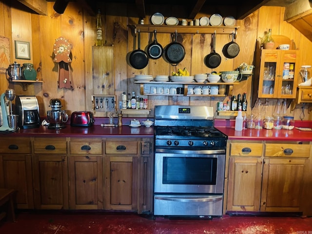 kitchen with beam ceiling, stainless steel range with gas stovetop, and wood walls