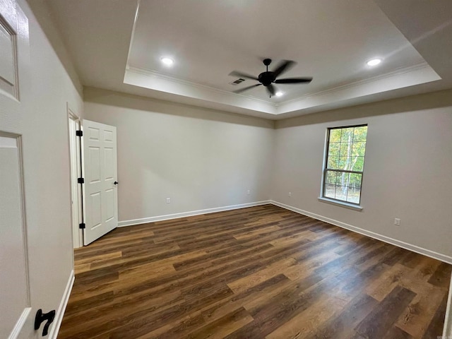 empty room with crown molding, a raised ceiling, and dark wood-style flooring