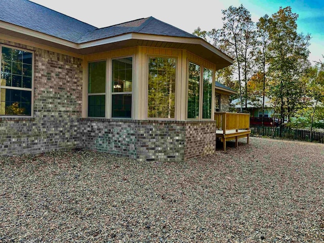 view of property exterior with a shingled roof, brick siding, and a wooden deck