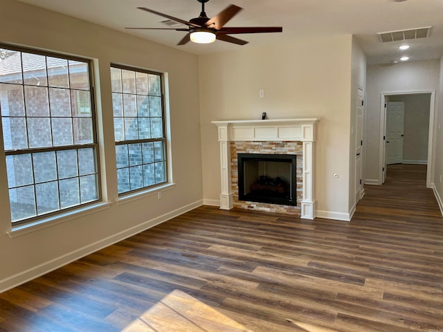 unfurnished living room with dark wood-type flooring, visible vents, plenty of natural light, and a stone fireplace