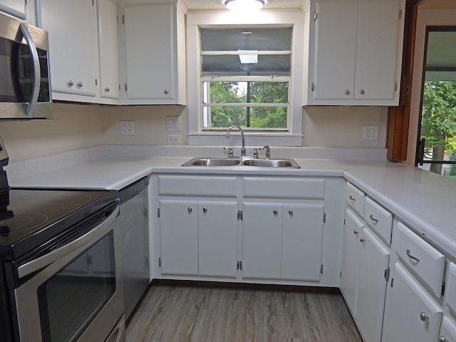 kitchen featuring light wood-style flooring, appliances with stainless steel finishes, light countertops, white cabinetry, and a sink