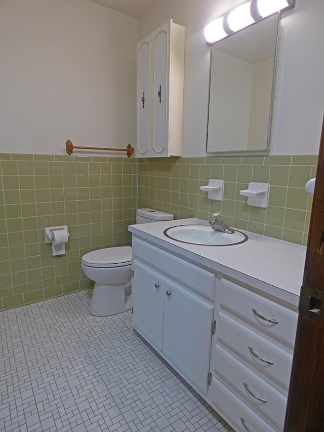 half bathroom with toilet, a wainscoted wall, tile patterned floors, vanity, and tile walls