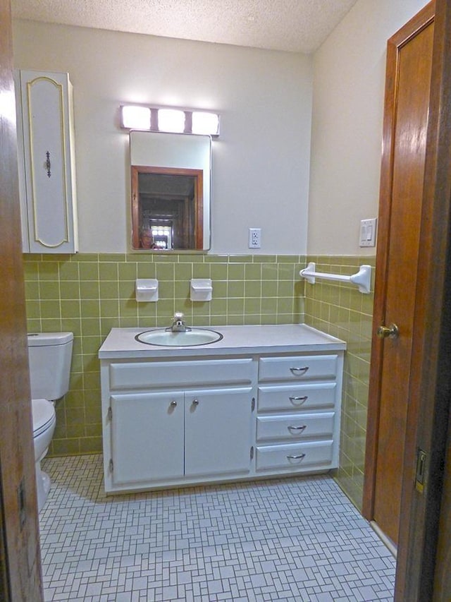 bathroom featuring a textured ceiling, tile patterned flooring, toilet, tile walls, and wainscoting