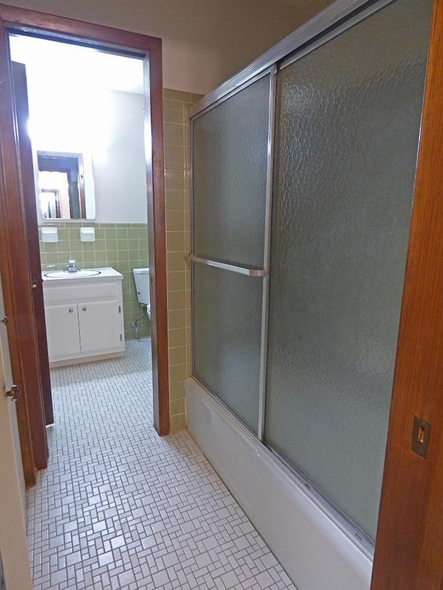 bathroom with toilet, vanity, tile walls, combined bath / shower with glass door, and wainscoting