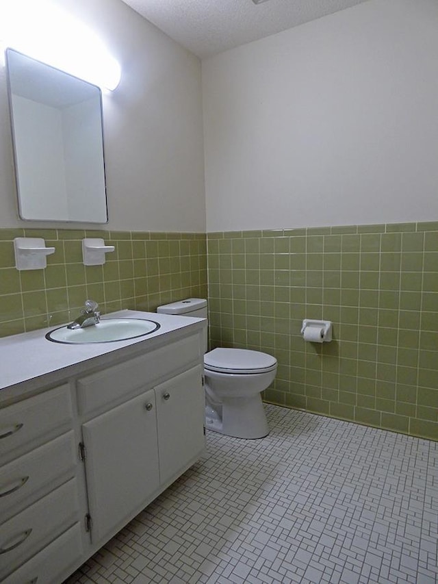 half bathroom featuring toilet, tile patterned flooring, tile walls, and vanity