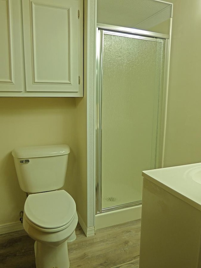 bathroom featuring baseboards, wood finished floors, toilet, and a shower stall