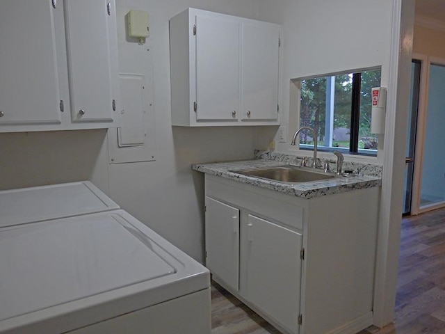 laundry area featuring washing machine and dryer, cabinet space, a sink, and light wood-style flooring