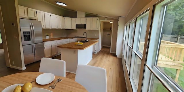 kitchen with stainless steel refrigerator with ice dispenser, vaulted ceiling, a kitchen island with sink, and white cabinets