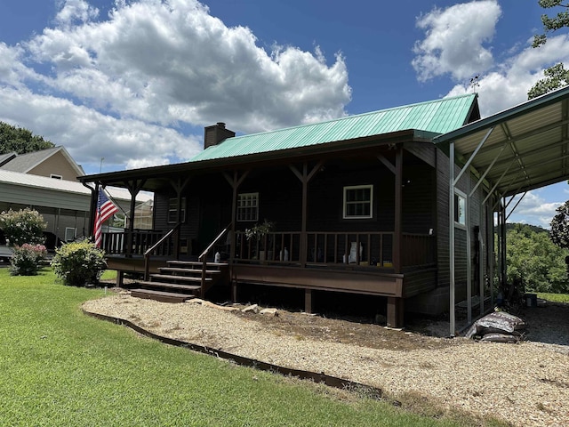 view of front of home featuring metal roof, covered porch, a carport, a chimney, and a front yard