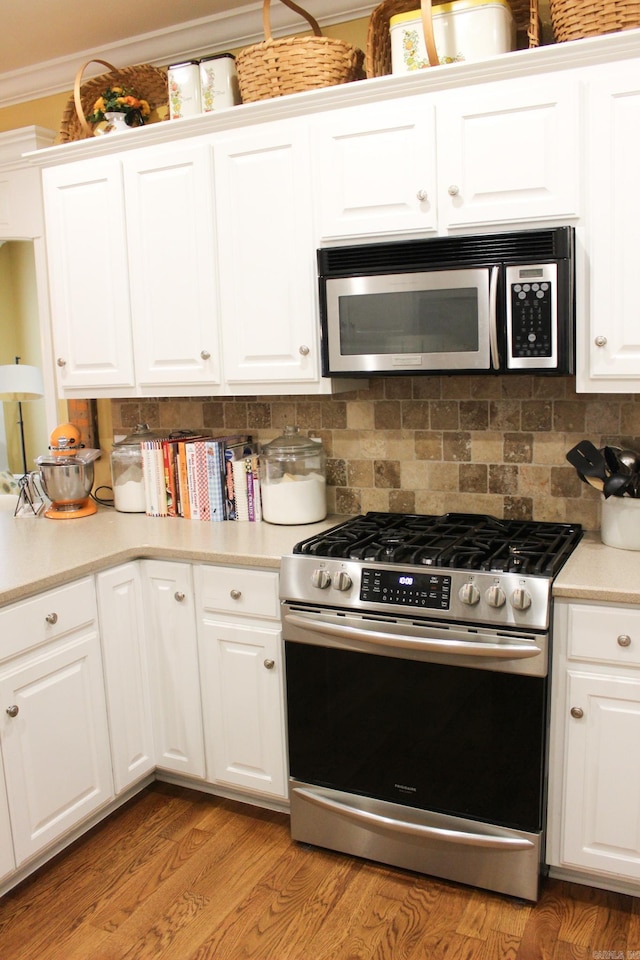 kitchen featuring stainless steel appliances, crown molding, white cabinets, light hardwood / wood-style floors, and backsplash