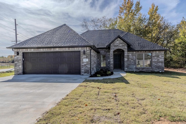 french country inspired facade featuring a garage, driveway, roof with shingles, a front lawn, and brick siding