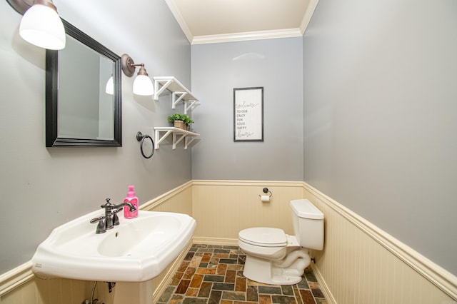 bathroom featuring toilet, a wainscoted wall, ornamental molding, and a sink