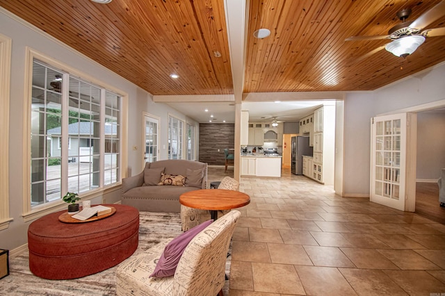 living area with light tile patterned floors, baseboards, wood ceiling, ceiling fan, and beamed ceiling