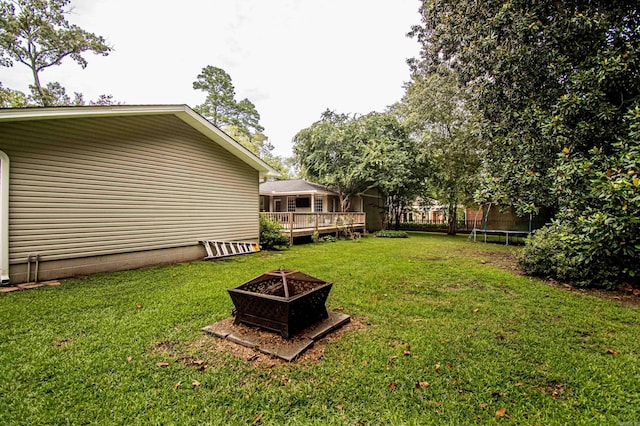 view of yard with a fire pit, a trampoline, and a wooden deck