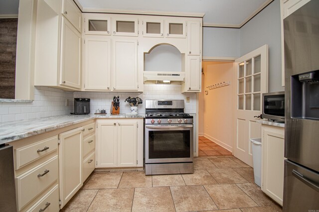 kitchen featuring appliances with stainless steel finishes, light tile patterned floors, decorative backsplash, light stone countertops, and wall chimney exhaust hood