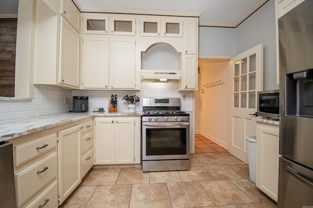 kitchen featuring light tile patterned floors, under cabinet range hood, appliances with stainless steel finishes, cream cabinetry, and tasteful backsplash