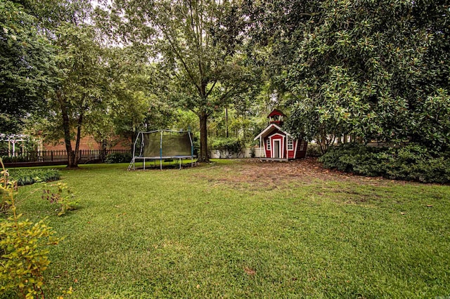 view of yard featuring an outbuilding, a trampoline, and fence