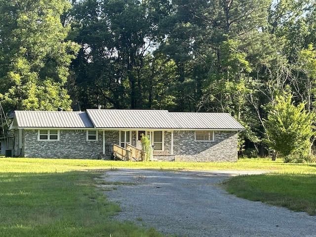 ranch-style home featuring metal roof, gravel driveway, covered porch, cooling unit, and a front lawn