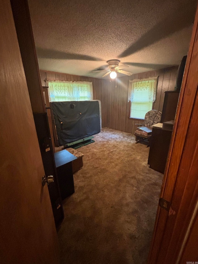 unfurnished bedroom with wooden walls, ceiling fan, carpet, and a textured ceiling