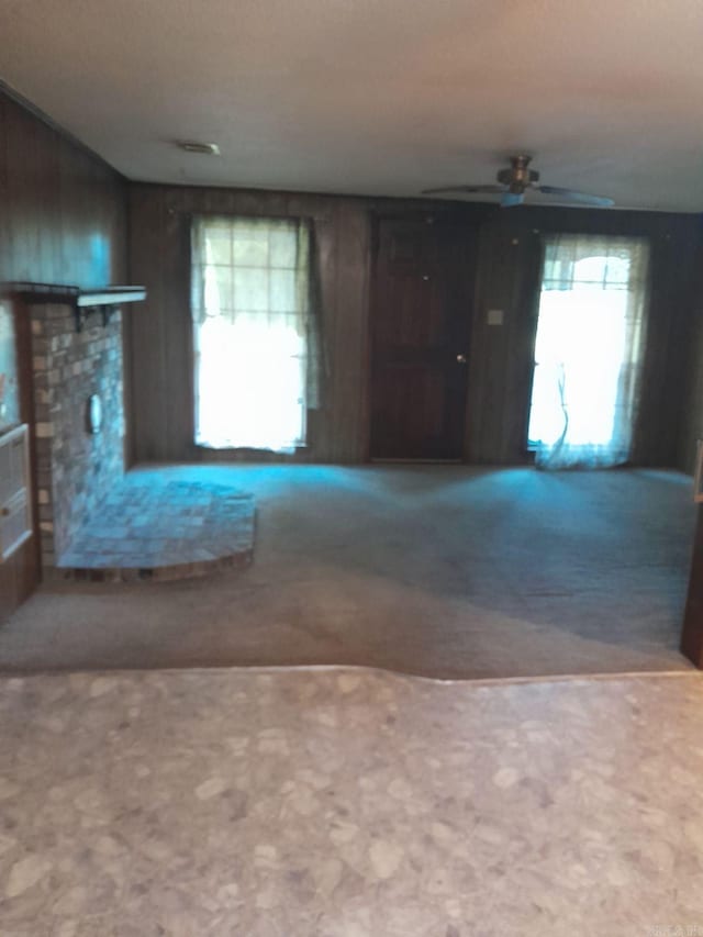 unfurnished living room with ceiling fan, wooden walls, and carpet flooring