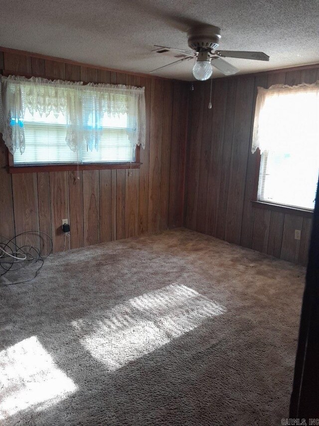 carpeted spare room with ceiling fan, a textured ceiling, and wooden walls