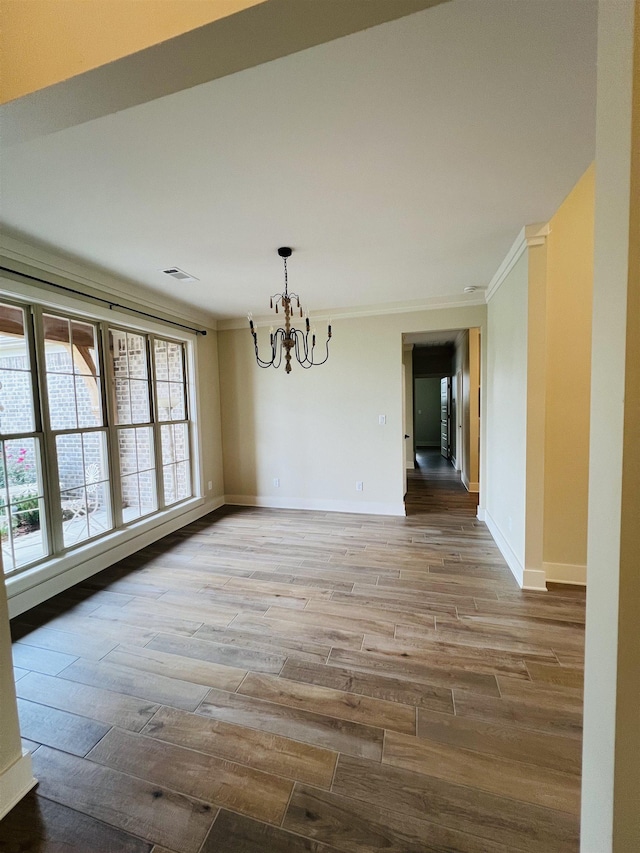 unfurnished dining area featuring ornamental molding, hardwood / wood-style floors, and a notable chandelier