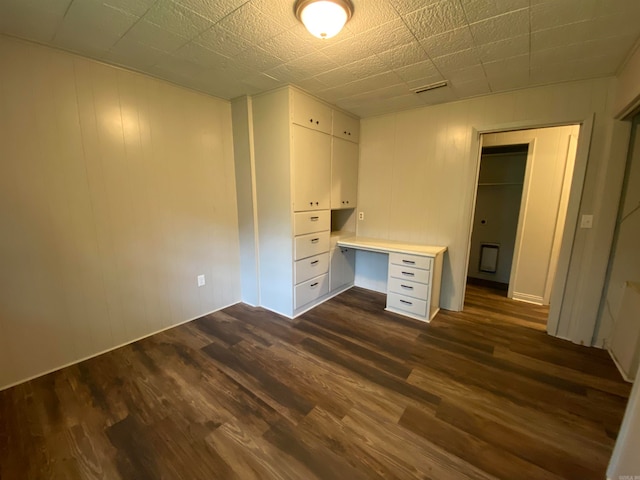 unfurnished office featuring dark hardwood / wood-style floors and built in desk