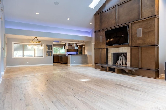 unfurnished living room featuring a tiled fireplace, sink, vaulted ceiling, and light hardwood / wood-style floors