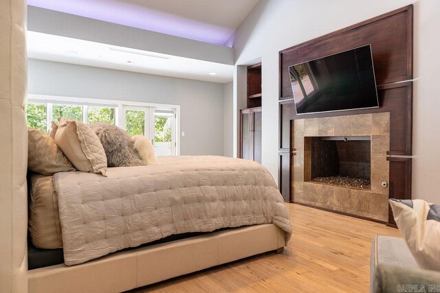 bedroom featuring a tiled fireplace, lofted ceiling, and light hardwood / wood-style floors