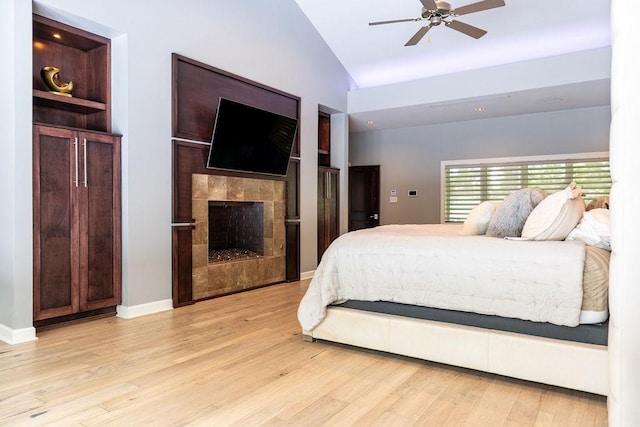 bedroom featuring lofted ceiling, a fireplace, ceiling fan, and light hardwood / wood-style flooring