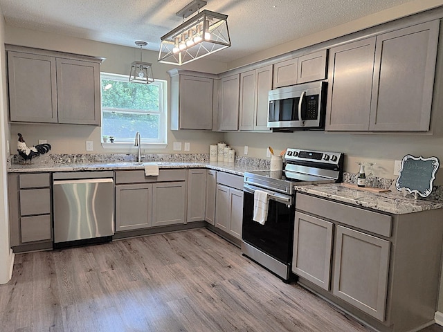 kitchen featuring gray cabinets, appliances with stainless steel finishes, light stone countertops, decorative light fixtures, and light wood-type flooring