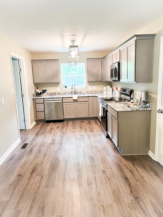 kitchen featuring light wood-type flooring, sink, a textured ceiling, stainless steel appliances, and light stone countertops