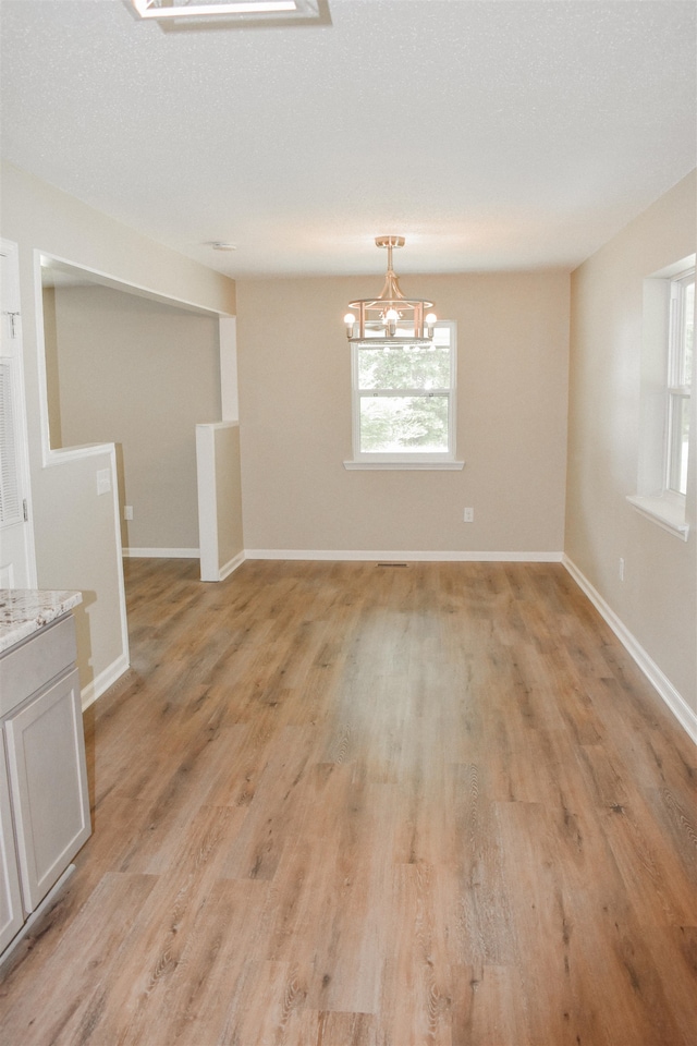 unfurnished room with a notable chandelier, a textured ceiling, light hardwood / wood-style flooring, and a wealth of natural light