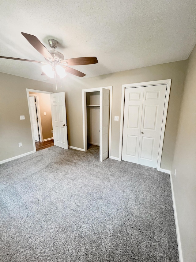 unfurnished bedroom featuring a textured ceiling, carpet flooring, two closets, and ceiling fan