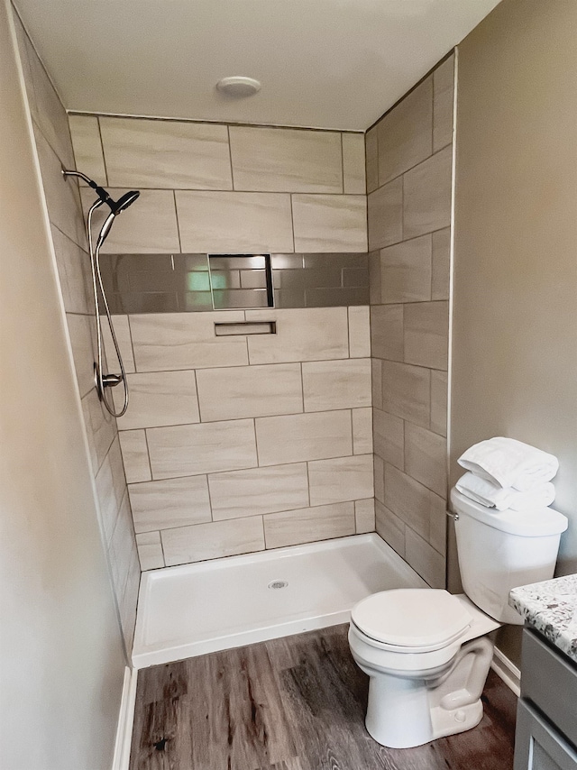 bathroom with a tile shower, vanity, hardwood / wood-style floors, and toilet