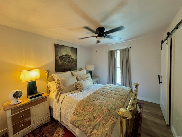 bedroom featuring dark hardwood / wood-style flooring, a barn door, and ceiling fan