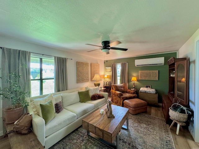 living room with hardwood / wood-style flooring, a textured ceiling, a wall mounted air conditioner, and ceiling fan