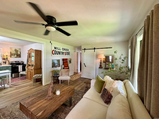 living room with a barn door, wood-type flooring, and ceiling fan