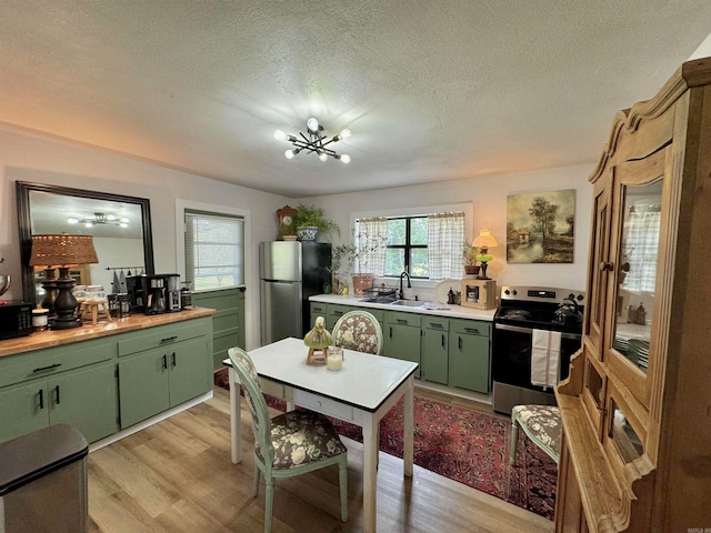 kitchen with green cabinets, a chandelier, stainless steel appliances, light wood-type flooring, and a textured ceiling