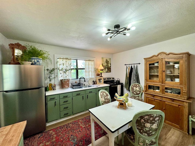 kitchen with appliances with stainless steel finishes, sink, green cabinets, a chandelier, and wood-type flooring