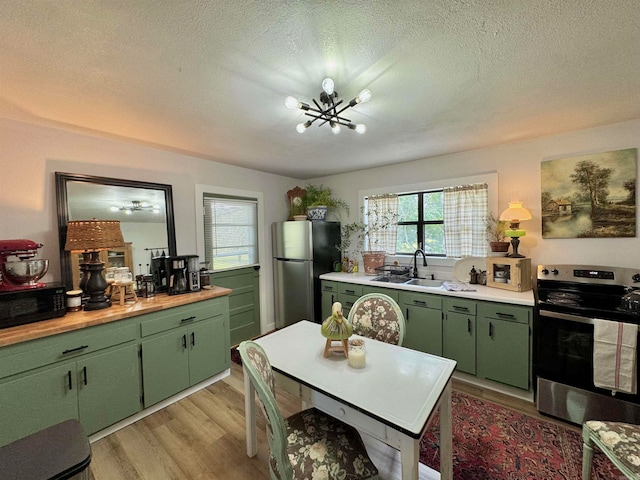 kitchen featuring appliances with stainless steel finishes, sink, light hardwood / wood-style floors, green cabinets, and a notable chandelier