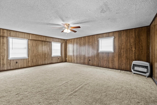 carpeted empty room with wood walls, ceiling fan, and a healthy amount of sunlight