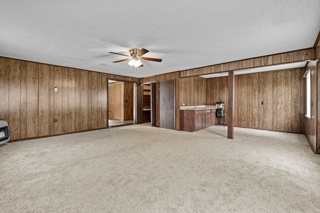 unfurnished room featuring light carpet, a textured ceiling, ceiling fan, and wooden walls