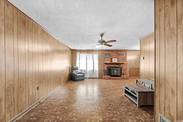 unfurnished living room featuring wood walls, a fireplace, ceiling fan, and a textured ceiling