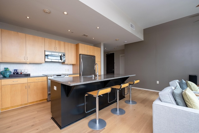 300 Third Unit 708, Little Rock, AR 72201 - kitchen with appliances with stainless steel finishes, light wood-style flooring, a breakfast bar area, decorative backsplash, and a kitchen island with sink