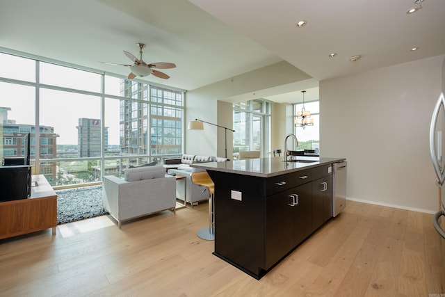 kitchen with sink, light wood-type flooring, ceiling fan with notable chandelier, and an island with sink