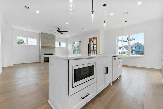 kitchen featuring built in microwave, sink, hanging light fixtures, a center island with sink, and white cabinets