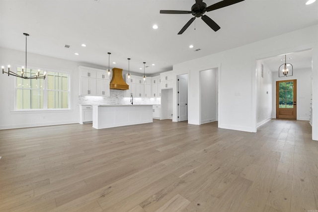 unfurnished living room with ceiling fan with notable chandelier, a healthy amount of sunlight, and light hardwood / wood-style floors