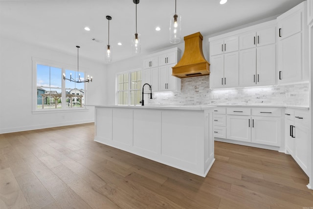 kitchen with white cabinetry, hanging light fixtures, a kitchen island with sink, decorative backsplash, and custom exhaust hood